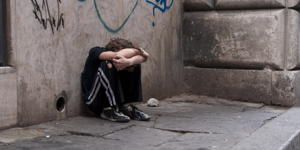 Boy huddled and alone on city street